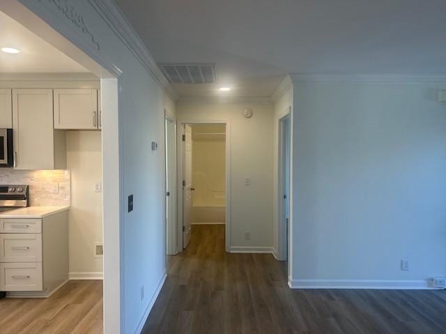 corridor featuring baseboards, visible vents, ornamental molding, and wood finished floors