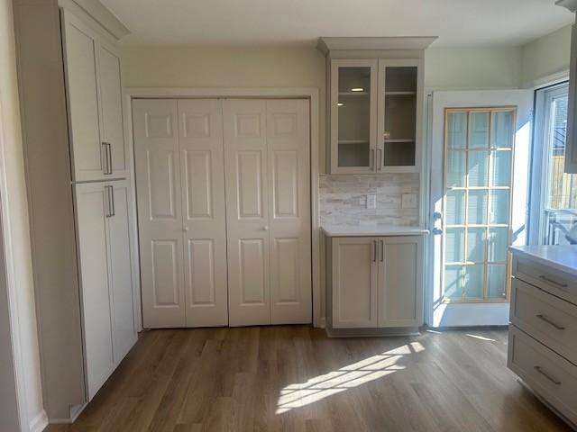 interior space featuring glass insert cabinets, light countertops, backsplash, and wood finished floors