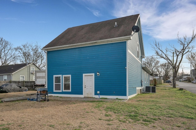 back of property featuring a shingled roof, fence, cooling unit, and a yard