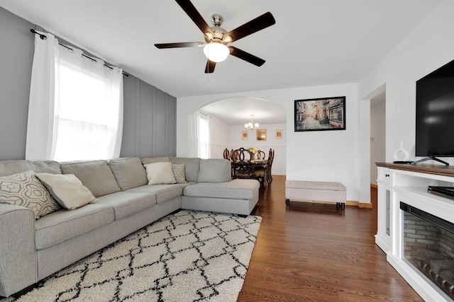 living area featuring a fireplace, arched walkways, wood finished floors, and ceiling fan with notable chandelier