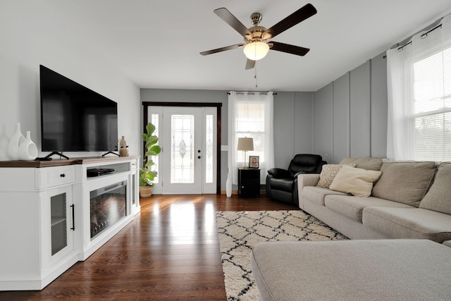 living area with a healthy amount of sunlight, ceiling fan, a fireplace, and dark wood finished floors