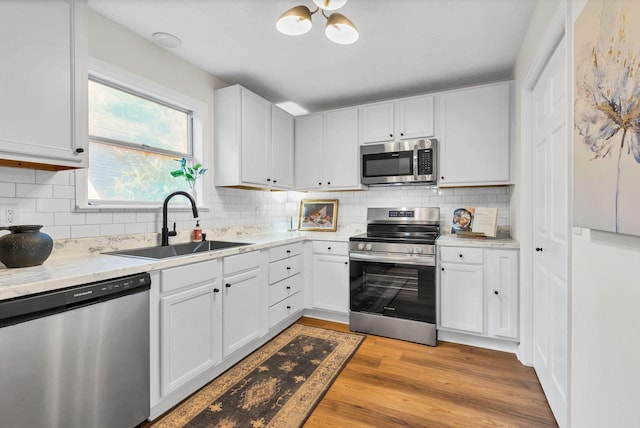 kitchen with light wood finished floors, appliances with stainless steel finishes, decorative backsplash, and a sink