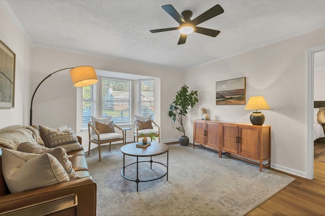 living room featuring a textured ceiling, baseboards, wood finished floors, and crown molding