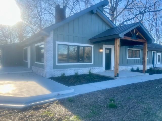 view of front of property with driveway, a chimney, board and batten siding, and brick siding