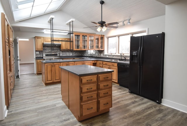 kitchen with dark countertops, a kitchen island, under cabinet range hood, black appliances, and a sink