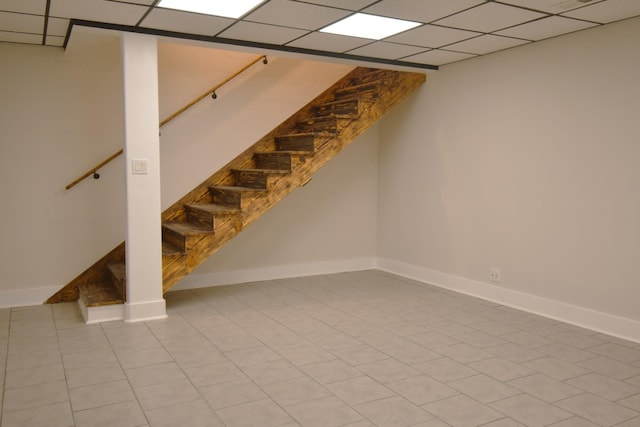 finished basement featuring tile patterned flooring, stairs, baseboards, and a drop ceiling