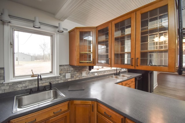 kitchen featuring decorative backsplash, dark countertops, a sink, and brown cabinets