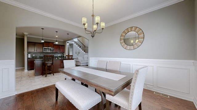 dining area with visible vents, arched walkways, a wainscoted wall, stairway, and an inviting chandelier