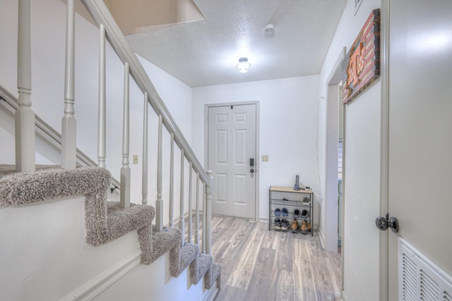 foyer entrance with visible vents, light wood-style flooring, a textured ceiling, and stairs