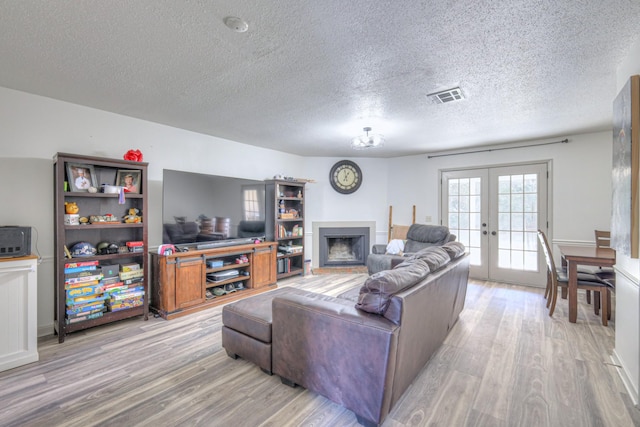 living area featuring french doors, a fireplace, visible vents, and light wood-style floors