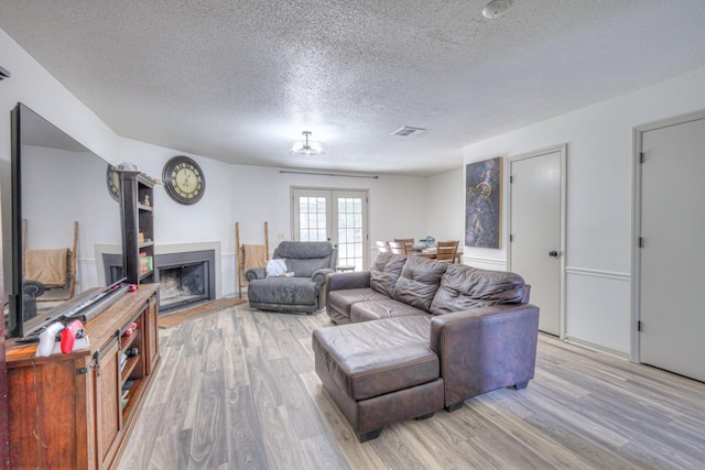 living room featuring french doors, visible vents, a fireplace, and light wood finished floors