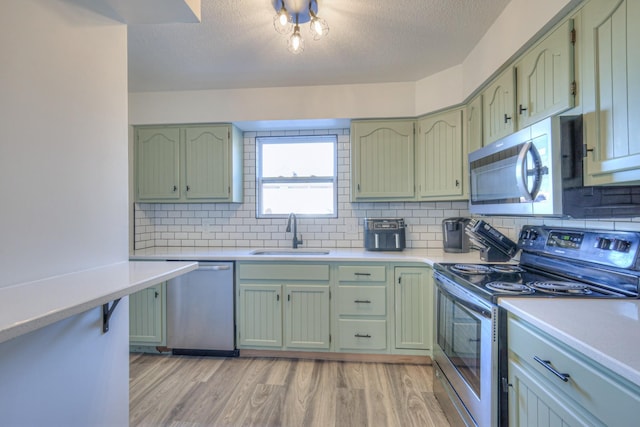 kitchen with light wood finished floors, appliances with stainless steel finishes, a sink, and green cabinetry