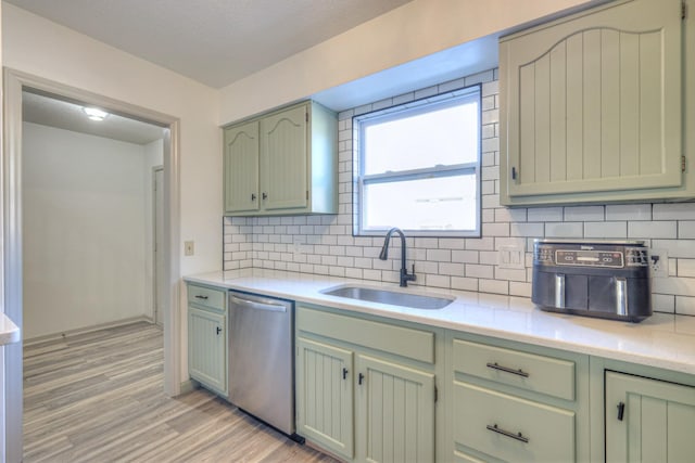 kitchen featuring dishwasher, light countertops, light wood-style floors, green cabinets, and a sink