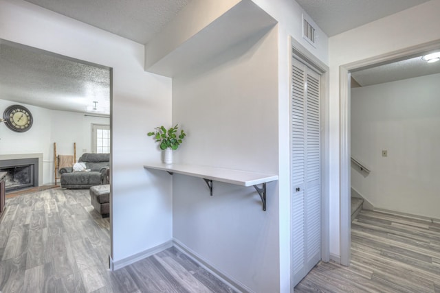 corridor featuring visible vents, a textured ceiling, baseboards, and wood finished floors