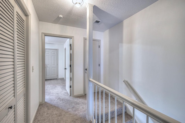 corridor with visible vents, carpet flooring, a textured ceiling, and baseboards