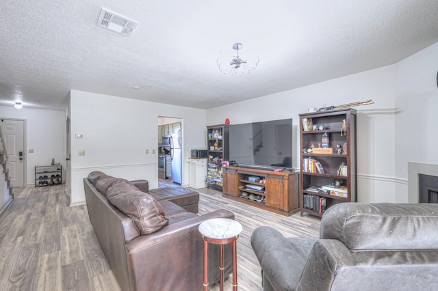 living area featuring light wood finished floors, visible vents, and a textured ceiling
