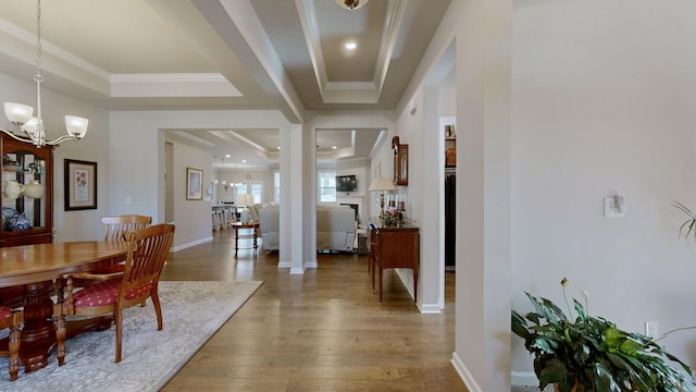 entryway featuring a tray ceiling, a notable chandelier, crown molding, wood-type flooring, and baseboards