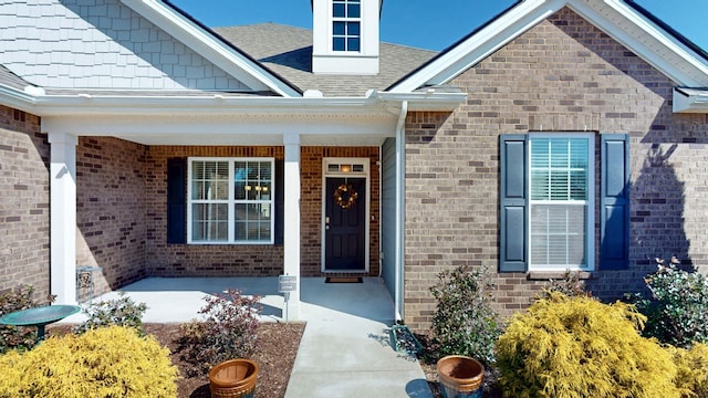 property entrance featuring covered porch, a shingled roof, and brick siding