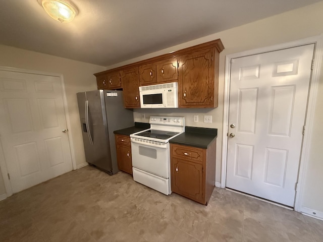 kitchen featuring dark countertops, white appliances, brown cabinets, and baseboards