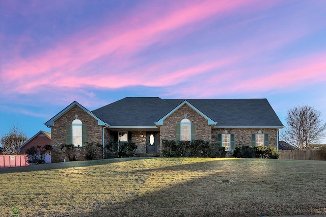 ranch-style home featuring roof with shingles, brick siding, a lawn, and fence