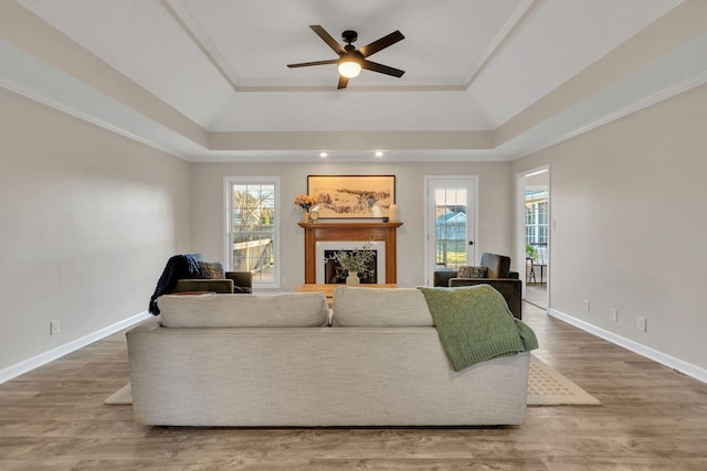 living area featuring a tray ceiling, a fireplace, ceiling fan, wood finished floors, and baseboards