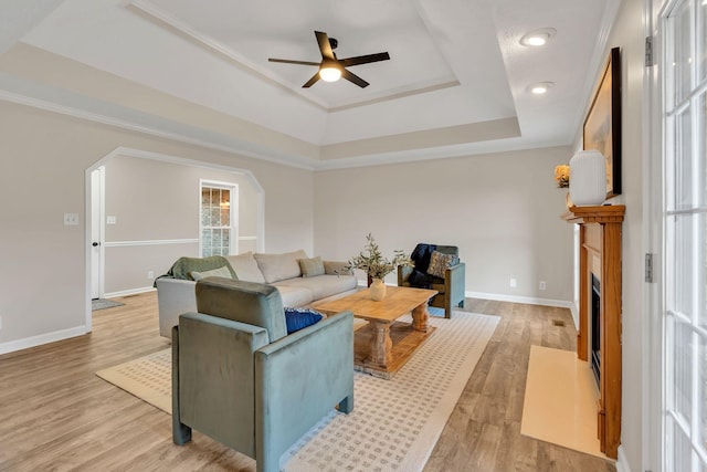 living area featuring light wood finished floors, arched walkways, a raised ceiling, baseboards, and a fireplace with flush hearth