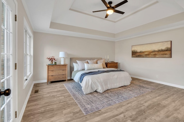 bedroom with wood finished floors, a raised ceiling, visible vents, and baseboards