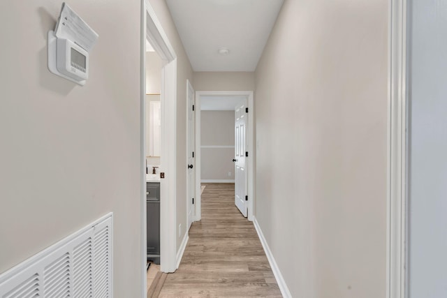 hallway featuring visible vents, light wood-style flooring, and baseboards