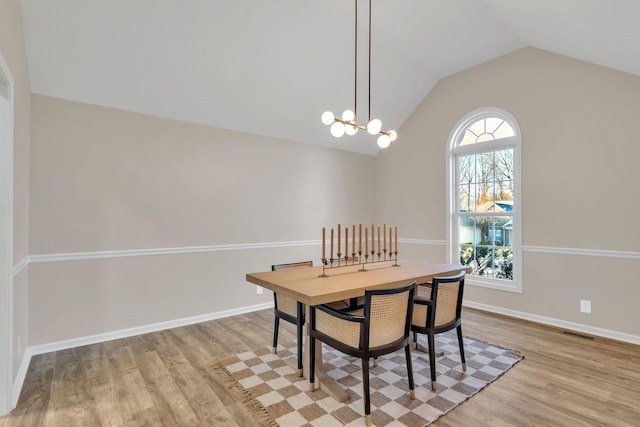 dining area featuring a notable chandelier, visible vents, vaulted ceiling, and wood finished floors