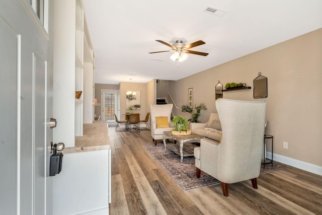 living area with ceiling fan with notable chandelier, wood finished floors, visible vents, and baseboards