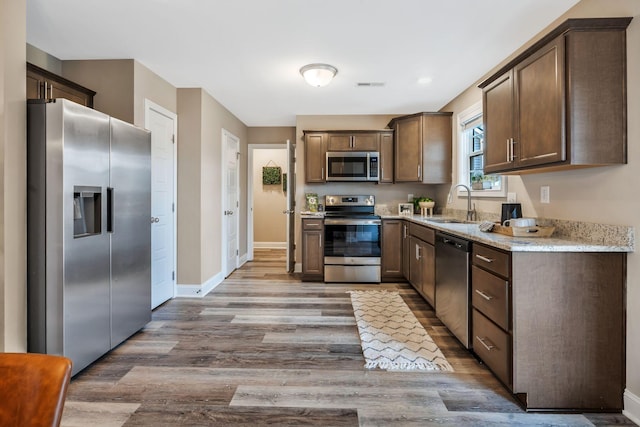 kitchen with light stone counters, wood finished floors, a sink, baseboards, and appliances with stainless steel finishes