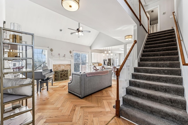 living area featuring high vaulted ceiling, a ceiling fan, a fireplace, and stairs