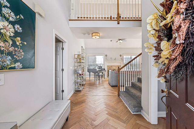 foyer entrance featuring baseboards, a ceiling fan, a towering ceiling, and stairs