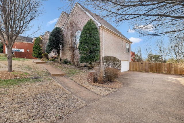 view of side of home featuring driveway, a garage, fence, and brick siding