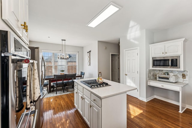 kitchen featuring dark wood-style flooring, light countertops, appliances with stainless steel finishes, white cabinetry, and a kitchen island