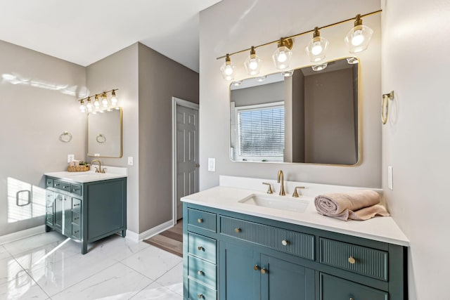 full bath featuring marble finish floor, baseboards, two vanities, and a sink