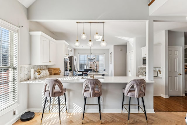 kitchen with a peninsula, a sink, light countertops, white cabinetry, and a notable chandelier