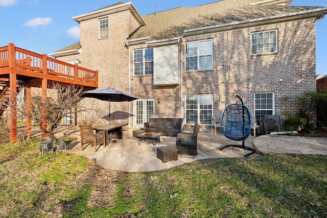 back of house featuring a shingled roof, a deck, a yard, a patio area, and brick siding