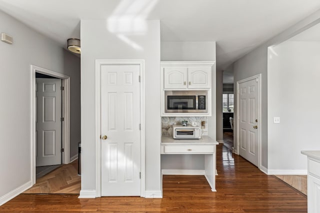 kitchen featuring light countertops, stainless steel microwave, white cabinetry, and baseboards