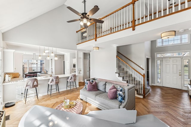 living room featuring baseboards, high vaulted ceiling, stairway, and a healthy amount of sunlight