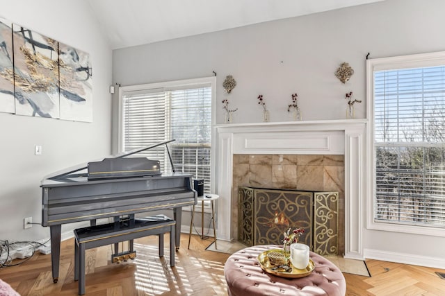 living area featuring light wood-type flooring, lofted ceiling, baseboards, and a tiled fireplace