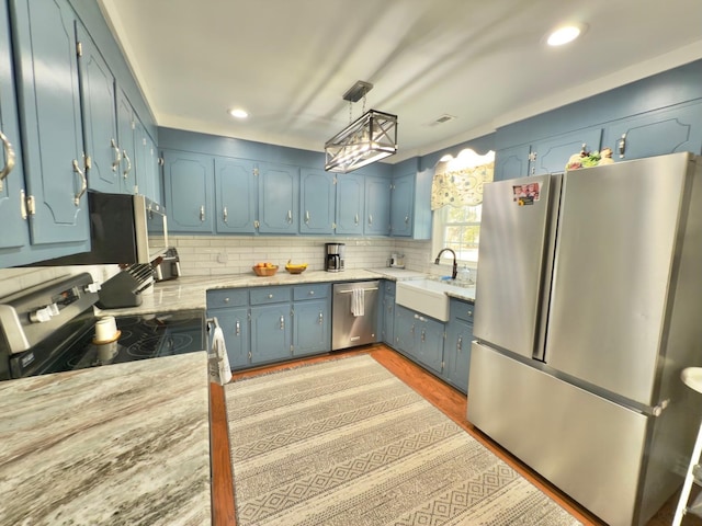 kitchen with stainless steel appliances, light countertops, backsplash, a sink, and blue cabinets