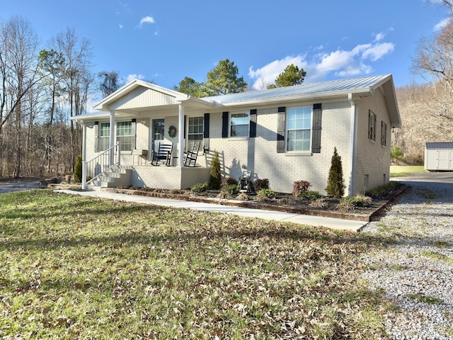 ranch-style home featuring driveway, metal roof, covered porch, a front lawn, and brick siding