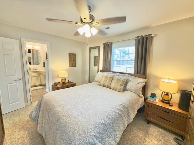 bedroom featuring connected bathroom, light colored carpet, visible vents, and ceiling fan