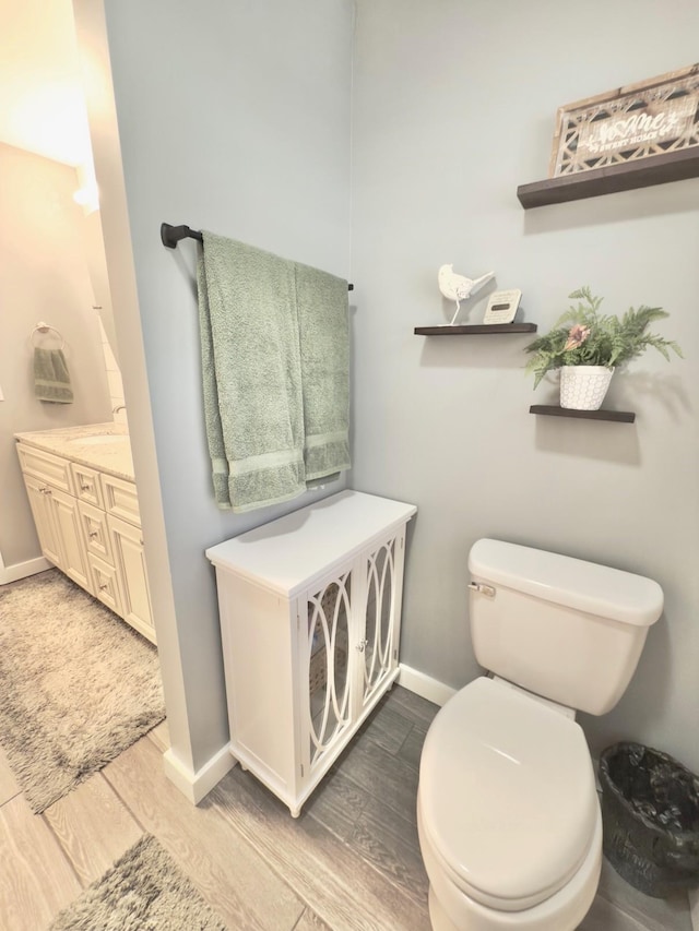 bathroom featuring toilet, baseboards, wood finished floors, and vanity