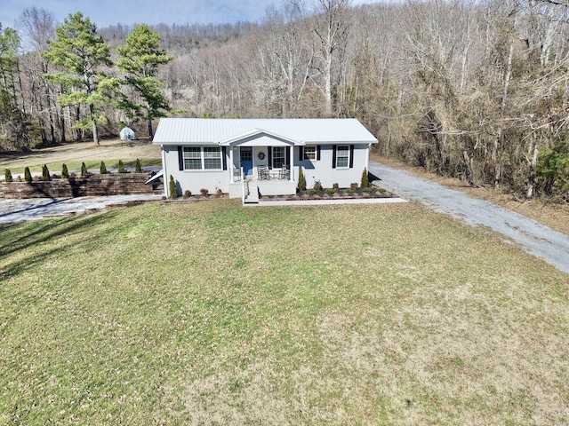 ranch-style house with metal roof, covered porch, driveway, a forest view, and a front lawn