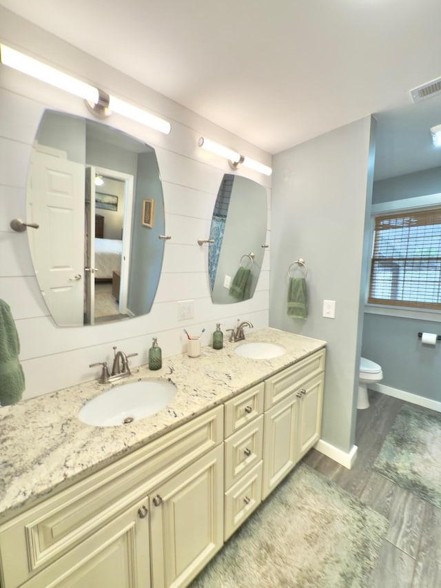 ensuite bathroom featuring double vanity, visible vents, a sink, and wood finished floors