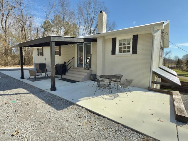 rear view of property featuring brick siding, a patio, and a chimney