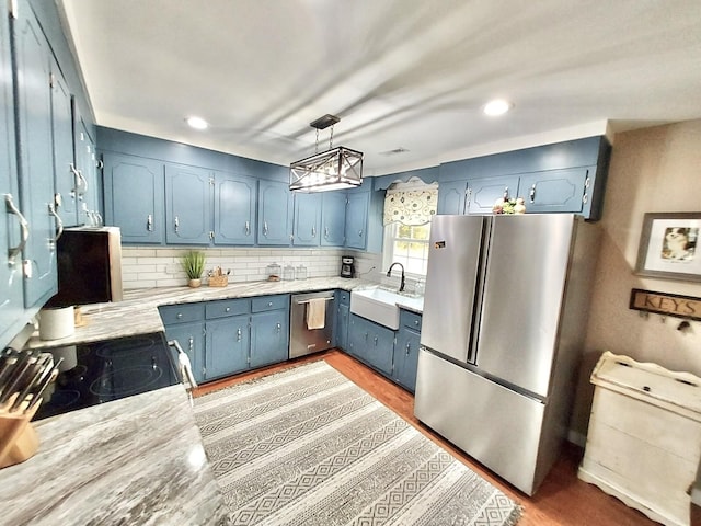 kitchen featuring blue cabinetry, stainless steel appliances, hanging light fixtures, backsplash, and a sink