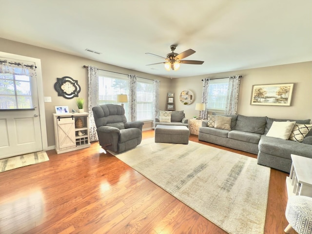 living area with ceiling fan, plenty of natural light, wood finished floors, and visible vents